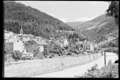 Ortschaft mit Kirche umgeben von hohen, bewaldeten Bergen