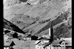 Ortschaft mit Kirche umgeben von hohen, bewaldeten Bergen
