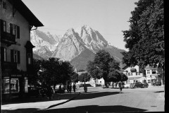 Ortschaft umgeben von hohen, bewaldeten Bergen und Grünfläche.