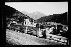 Kapelle/Anwesen umgeben von hohen, bewaldeten Bergen und Grünfläche.