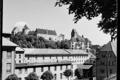 Ortschaft umgeben von bewaldeten Bergen mit Türmen.