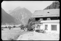 Großes Haus mit Terrasse mit Tischen und Stühlen, daneben ein Holzstall und der Wald