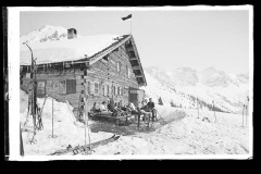 Hölzerne Skihütte, mit viel Skiequipment und Menschen vor den Dreischafsalpköpfen