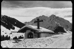 Kleine; verschneite Kapelle; mit hölzernem Kreuz und Aufschrift; dahinter der Widderstein;