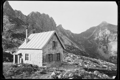 Gekachelte Almhütte, umgeben von Bergen, steiler Berggrat