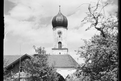Blick durch Bäume auf eine Kapelle mit Zwiebeldach, umgeben von blühenden Kirschbäumen