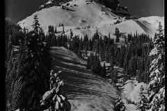 Verschneite Almhütte umgeben von karg bewaldete Berggipfeln, flaches Berg Plateau