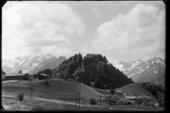 Kapelle (?) Auf einem bewaldete Hügel, umgeben von hölzernen Wohnhäusern, dahinter noch verschneite Berggipfel	auf bewaldeten Hügel