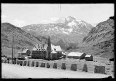 Großes, prunkvolles Anwesen mit Zwiebeldach, inmitten einer Wiese mit kleinem Schuppen nebenan, umgeben von Grünfläche, Hügeln und leicht verschneiten Bergen