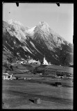 Ortschaft mit Kirche umgeben von hohen, bewaldeten Bergen