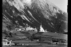 Ortschaft mit Kirche umgeben von hohen, bewaldeten Bergen