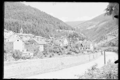 Ortschaft mit Kirche umgeben von hohen, bewaldeten Bergen