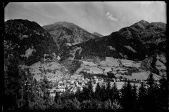 Ortschaft mit Zentrum und Kirche von Wald und Bergen umgeben, bewölkter Himmel