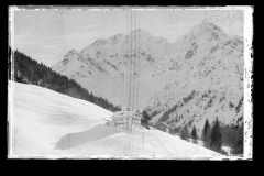 Wohnhaus und Holzhütte auf einem verschneiten Feld mit Skispuren vor dem Widderstein
