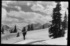 Skiläufer der auf steile Berge zugeht, blickt über die Schulter, auf verschneitem Feld, durchzogen von Skispuren