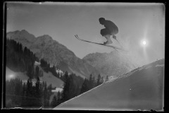 Skispringer führt einen Kunstsprung aus dahinter hohe, verschneite Berge, bewaldet und der klarer Himmel