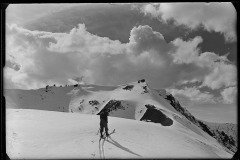 Männlicher, erwachsener Skifahrer auf einem beschneiden Gipfel, Blick auf Berggipfel und dahinter der bewölkte Himmel