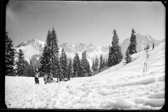 Schneelandschaft mit Skifahrern und Spuren im Schnee vor dem Wald und Bergen