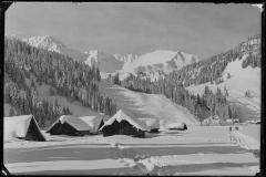 Schneelandschaft mit Skifahrern und Spuren im Schnee vor dem Wald und Bergen